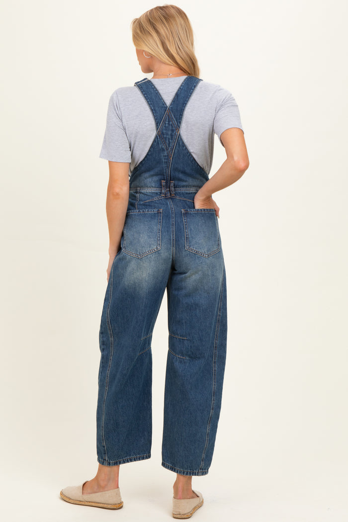 woman wearing a dark wash denim maternity overall with a loose fit and crossed back straps, showing a casual style