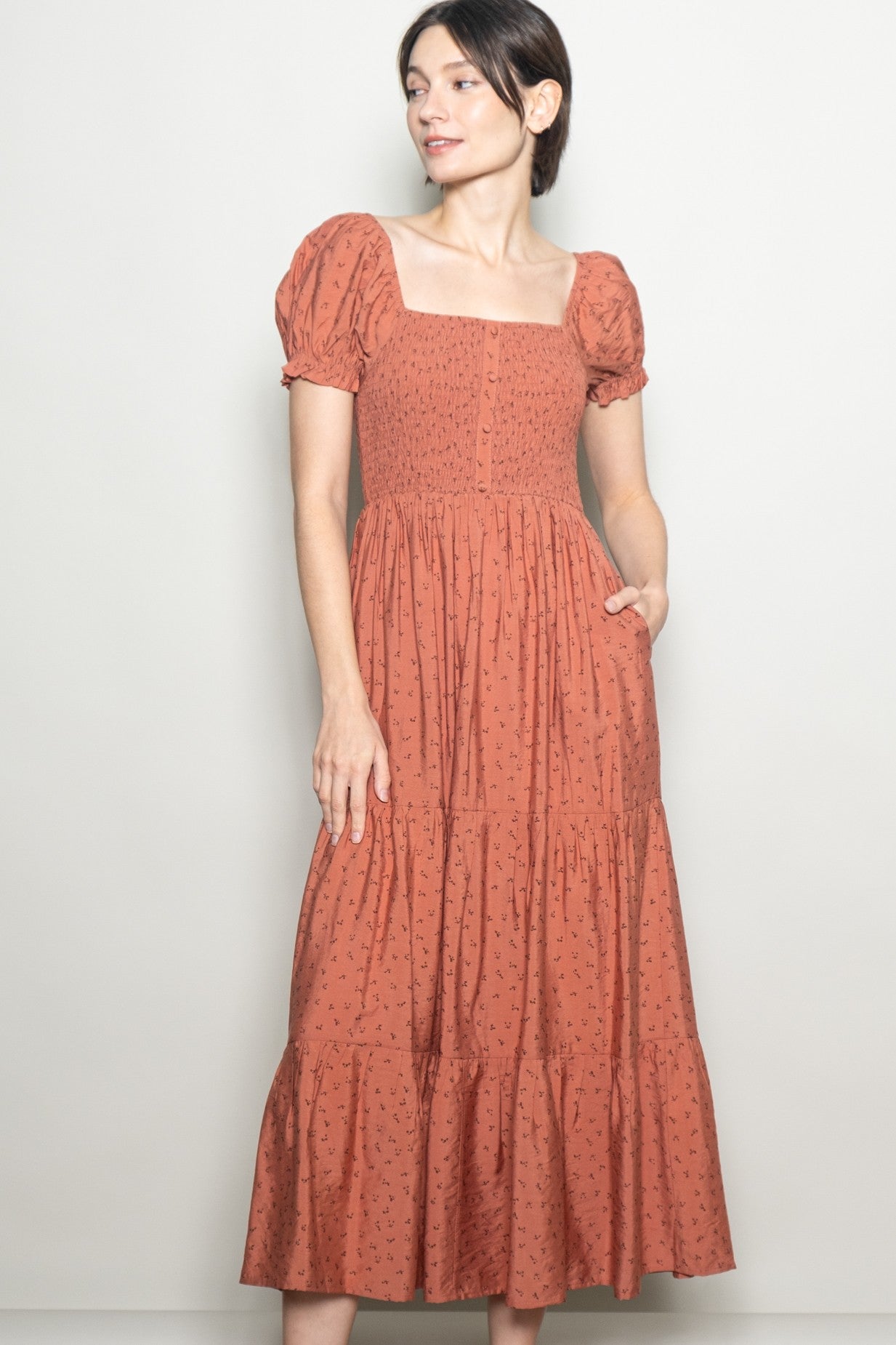 woman wearing a rust-colored puff sleeve maxi dress with a square neckline and floral pattern