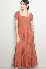woman wearing a rust-colored puff sleeve maxi dress with a square neckline and floral pattern