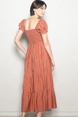 woman wearing a rust colored floral maxi dress with puff sleeves and a smocked bodice, viewed from the back