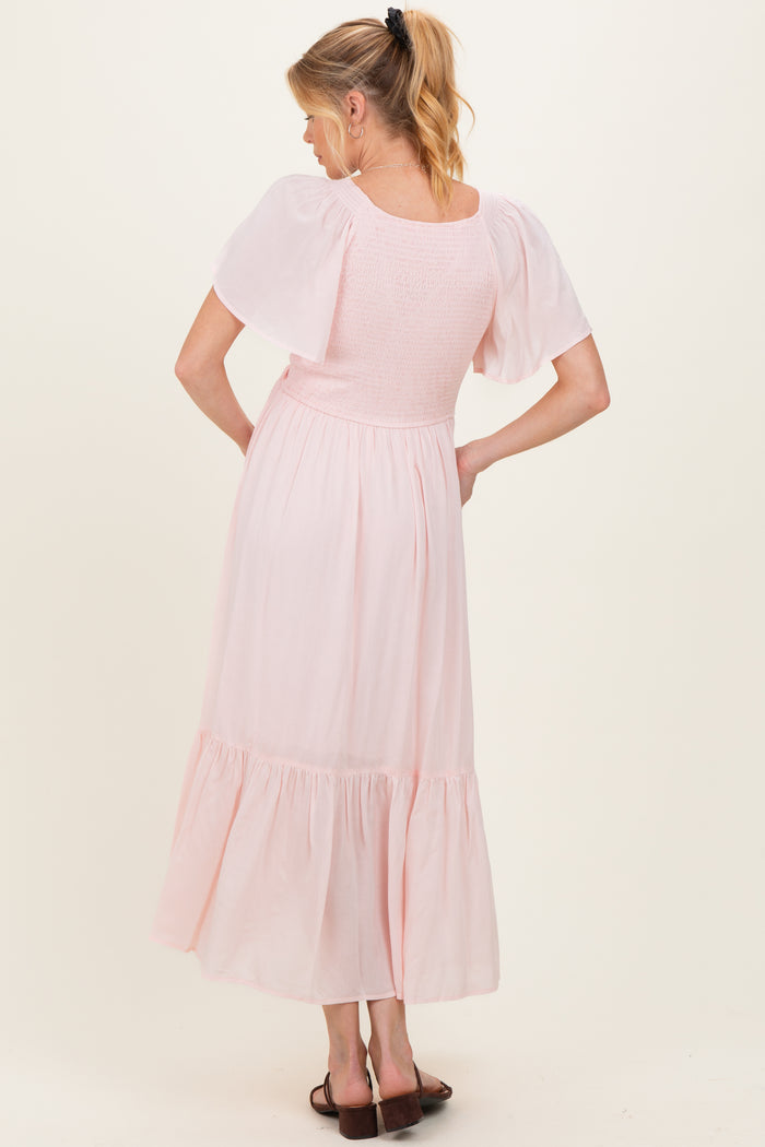 woman wearing a light pink maternity maxi dress with puff sleeves and smocked bodice, showing a baby bump from the back