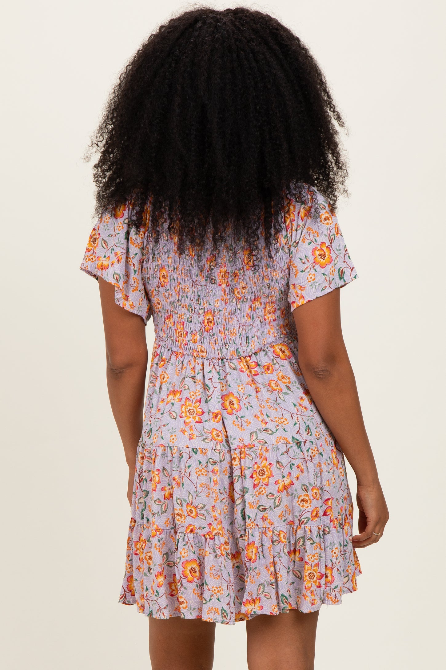 woman wearing a floral print short dress with a smocked back and ruffled hem standing with her back to the camera