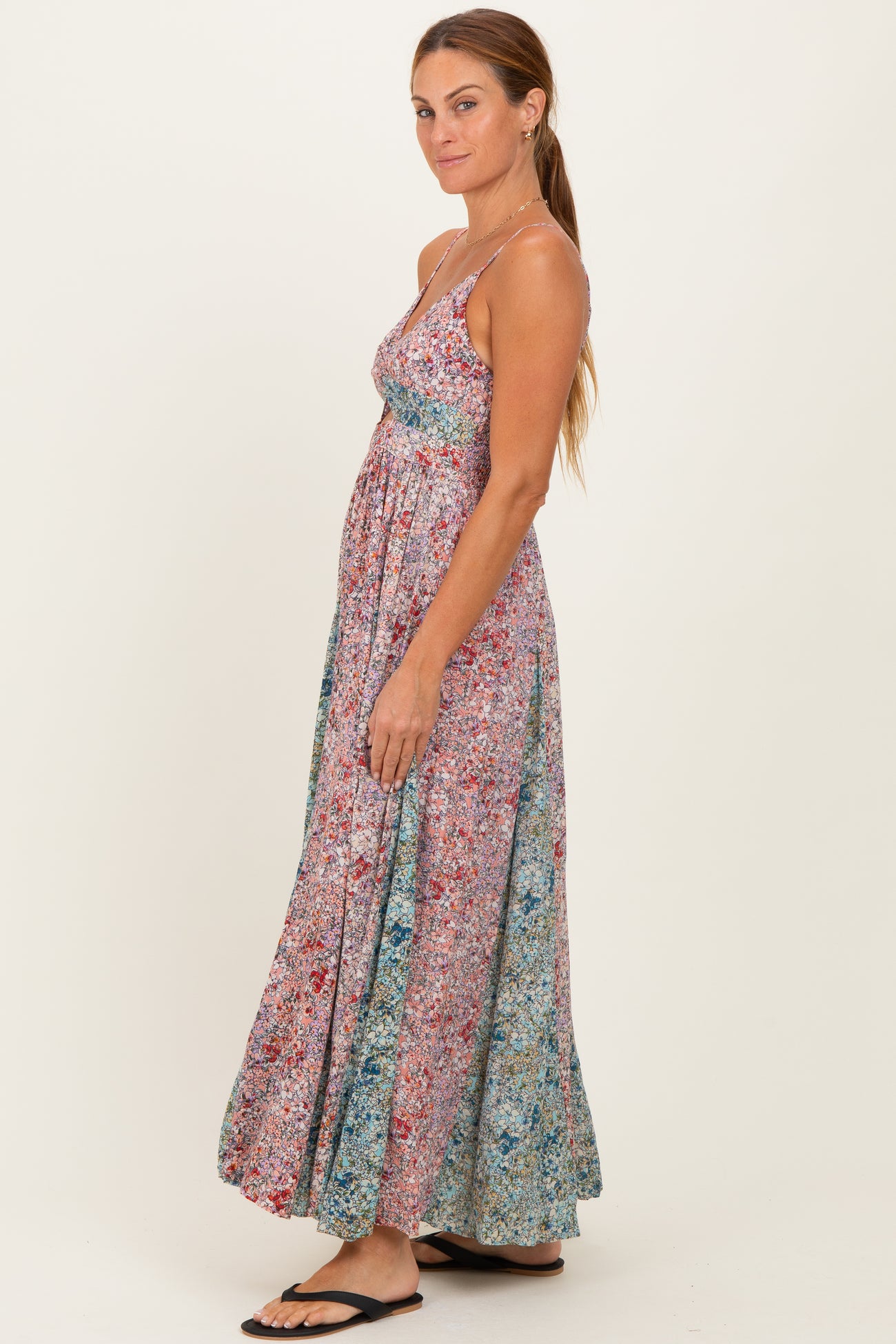 woman wearing a colorful floral maxi dress with a fitted bodice and flowy skirt, standing sideways