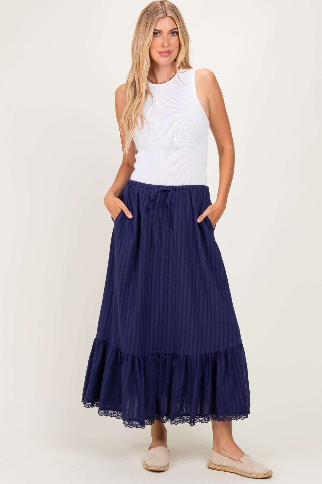woman wearing a white sleeveless top and a long navy blue skirt with pockets and lace trim