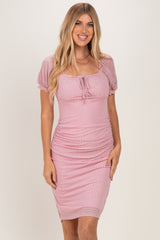 woman wearing a pink polka dot fitted dress with short puff sleeves and a tie detail at the neckline