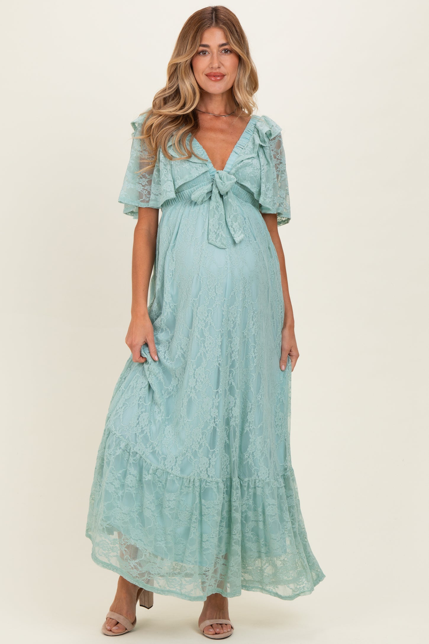 woman wearing a light blue lace maternity dress with a tie front and flutter sleeves, showing her baby bump