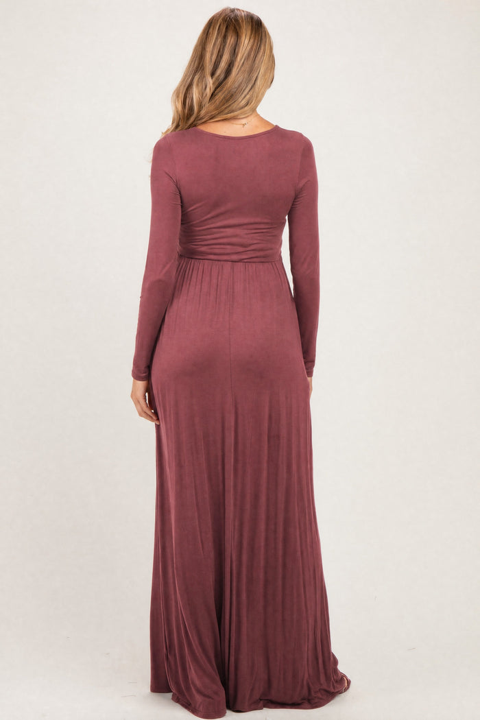 woman wearing a burgundy long sleeve maternity maxi dress with a fitted waist and flowing skirt, view from the back