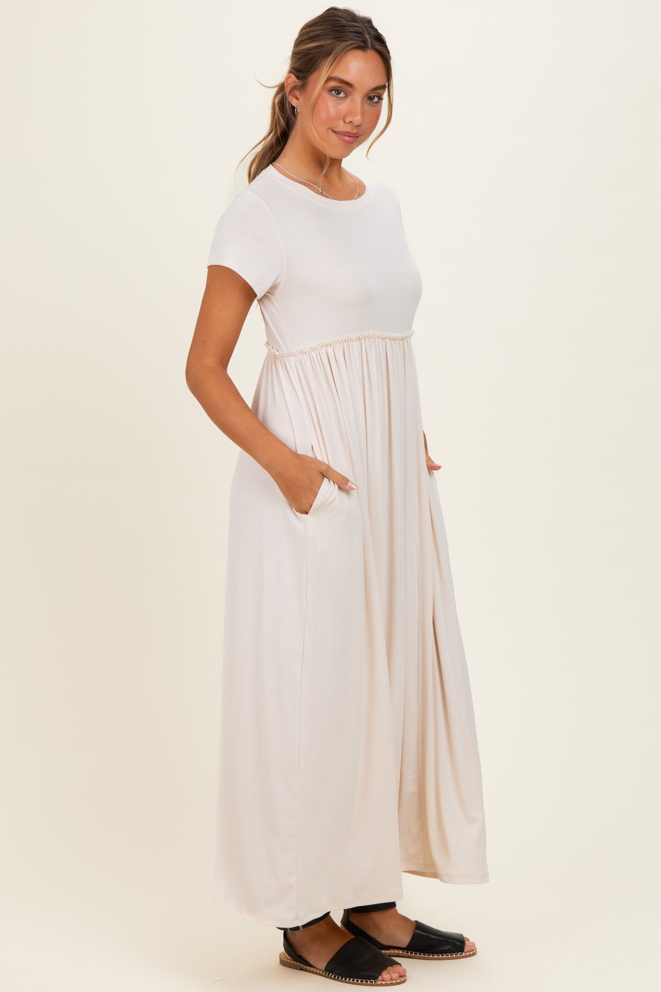 woman wearing a beige short sleeve maxi dress with a gathered waist and pockets, styled casually