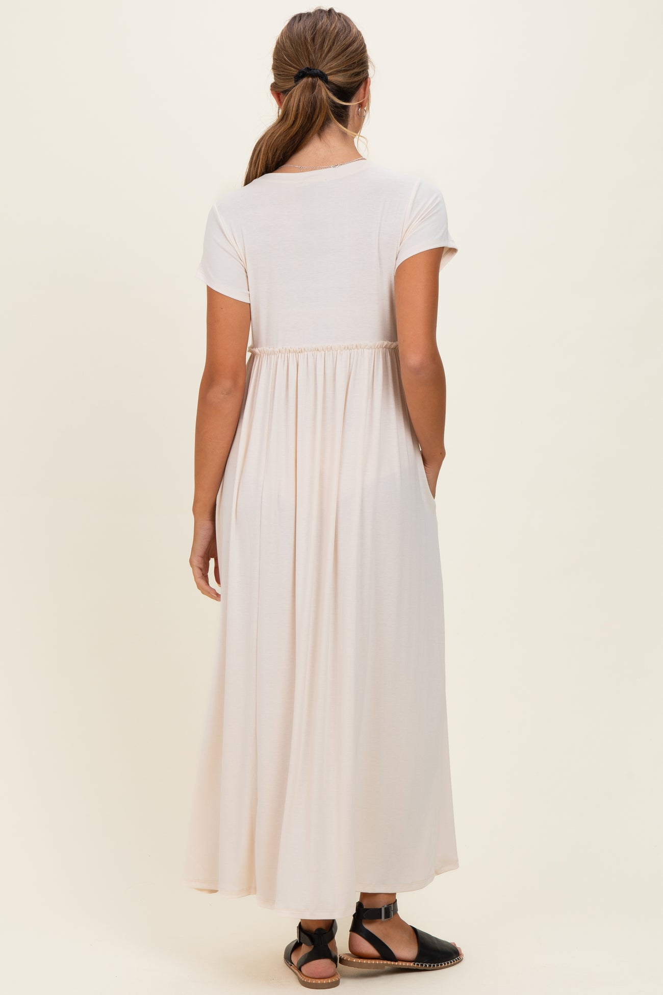 woman wearing a light pink short sleeve maxi dress with a gathered back and side pockets