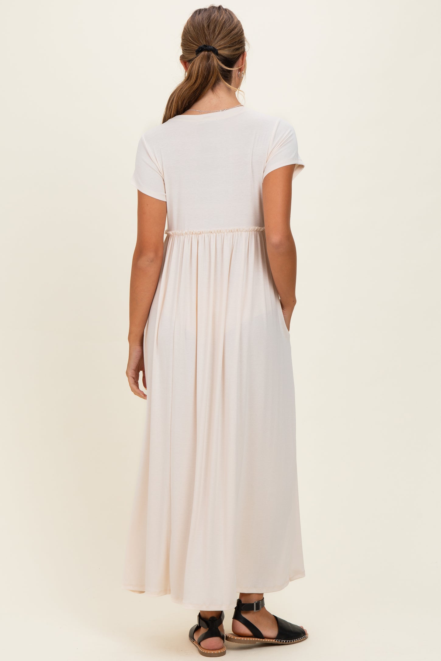 woman wearing a light pink short sleeve maxi dress with a gathered back and side pockets