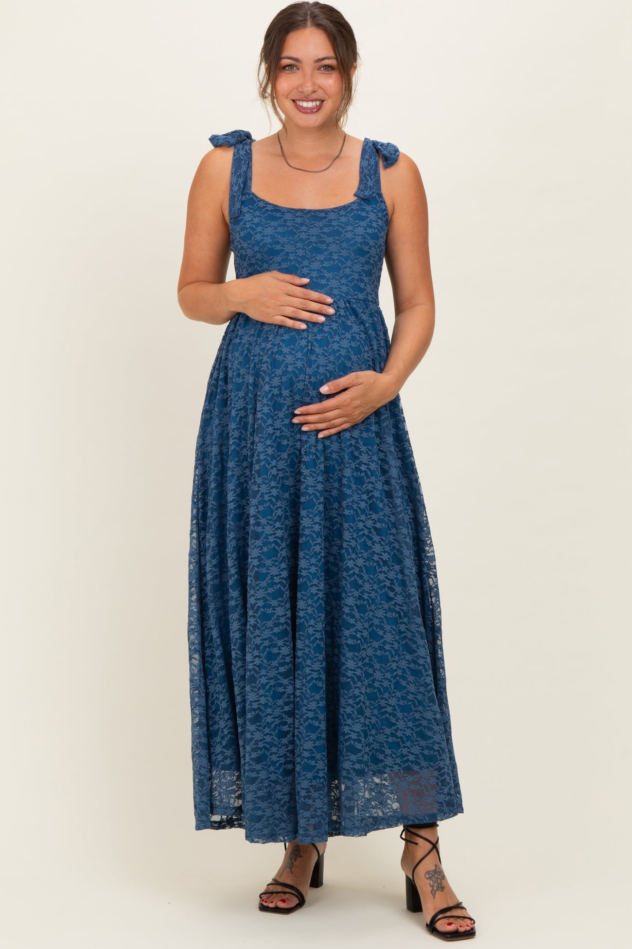 woman wearing a dark blue lace maternity dress with tie straps and holding her baby bump