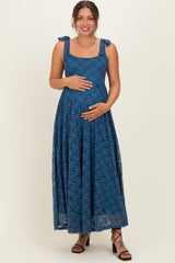 woman wearing a dark blue lace maternity dress with tie straps and holding her baby bump