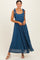 woman wearing a dark blue maxi dress with tie straps and a flowy skirt, standing and smiling