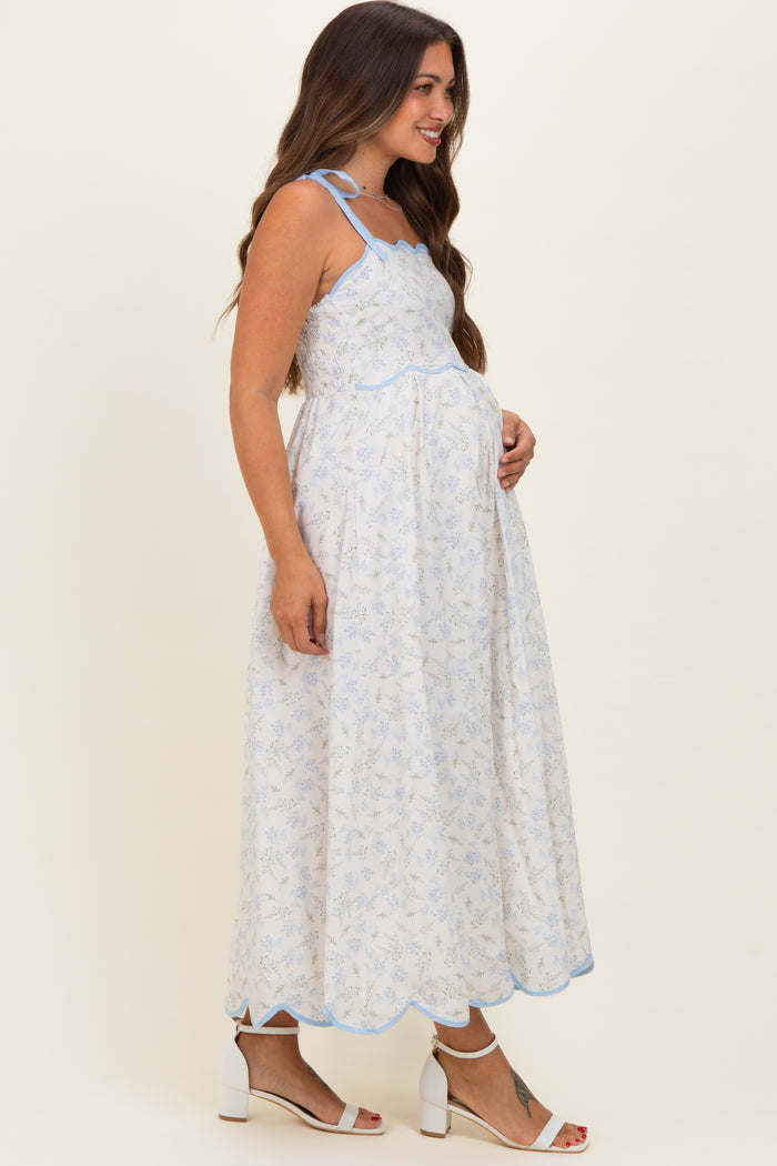woman wearing a white floral maternity dress with blue scalloped details, holding her baby bump
