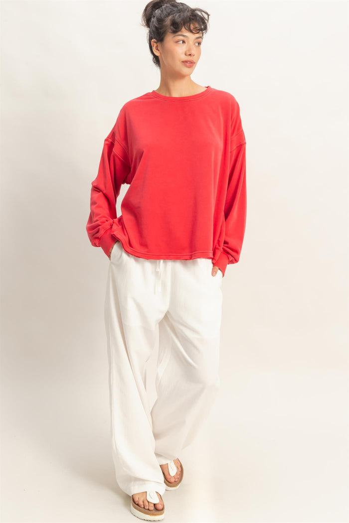 woman wearing a red oversized sweatshirt and white wide-leg pants, standing with hands in pockets