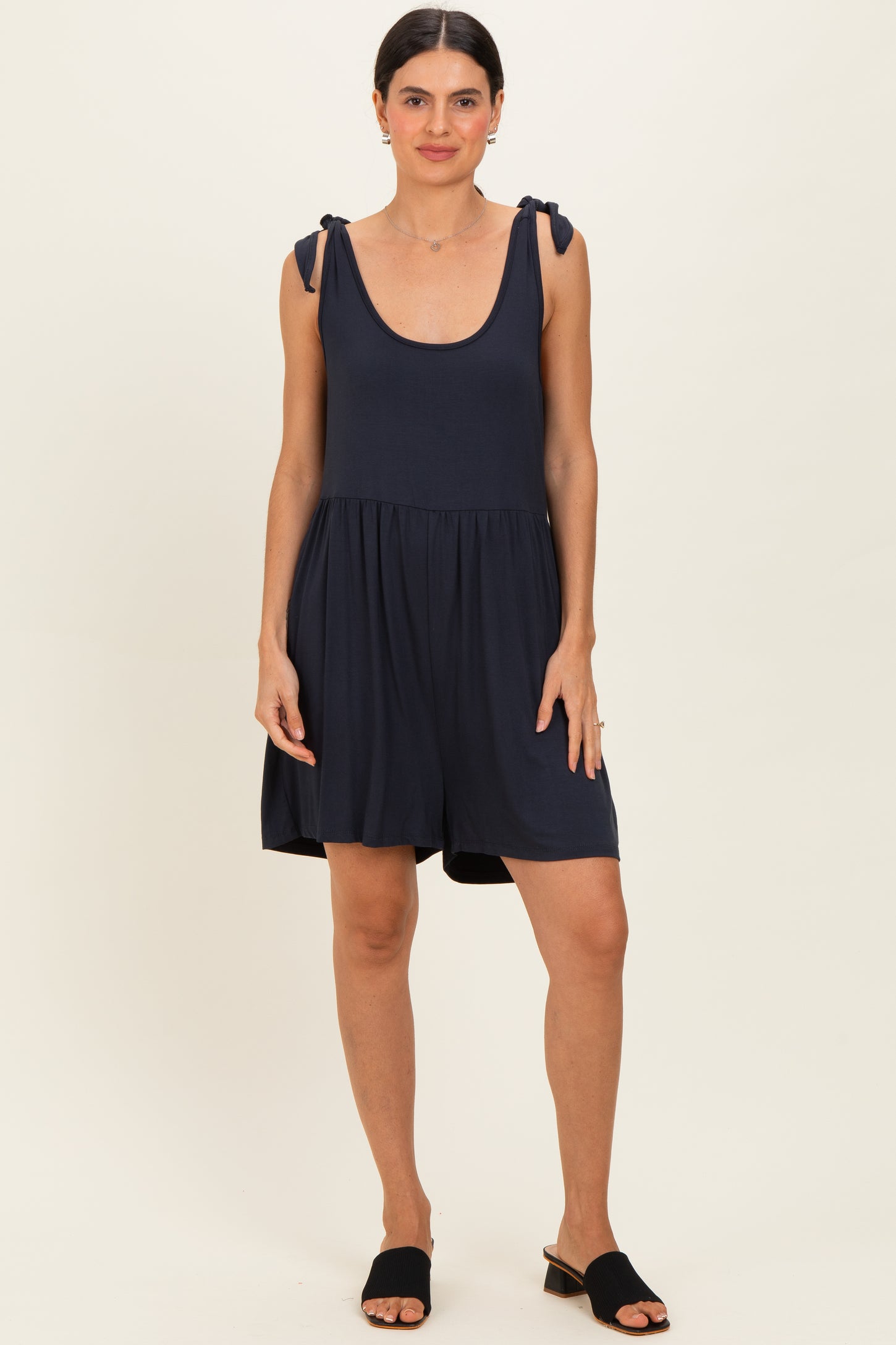 woman wearing a navy blue sleeveless romper with tie straps and a flared skirt, standing casually