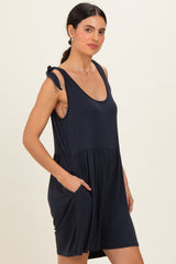 woman wearing a navy blue sleeveless dress with a gathered waist and side pockets, featuring tie detail on the straps