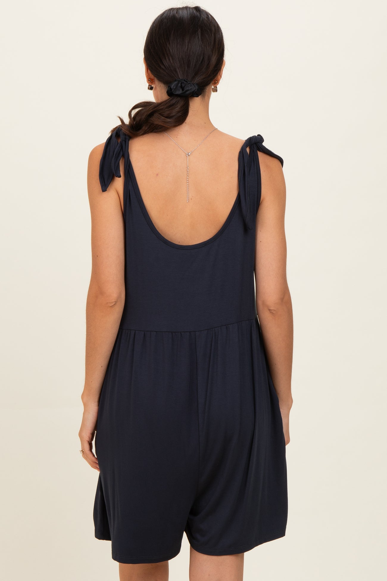 woman wearing a navy blue sleeveless romper with tie straps and a relaxed fit from the back