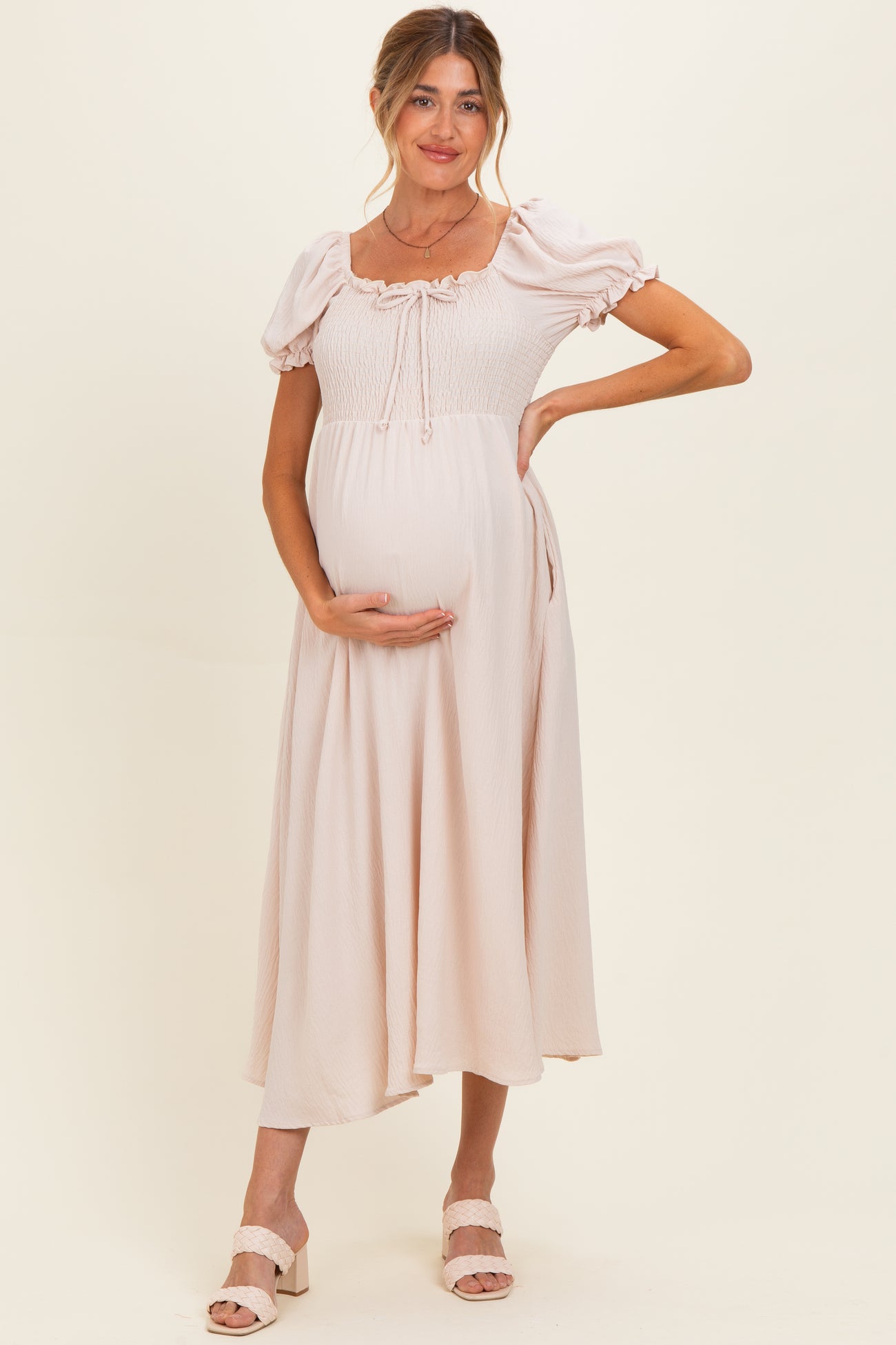woman wearing a light pink maternity dress with puff sleeves and a smocked bodice, holding her baby bump