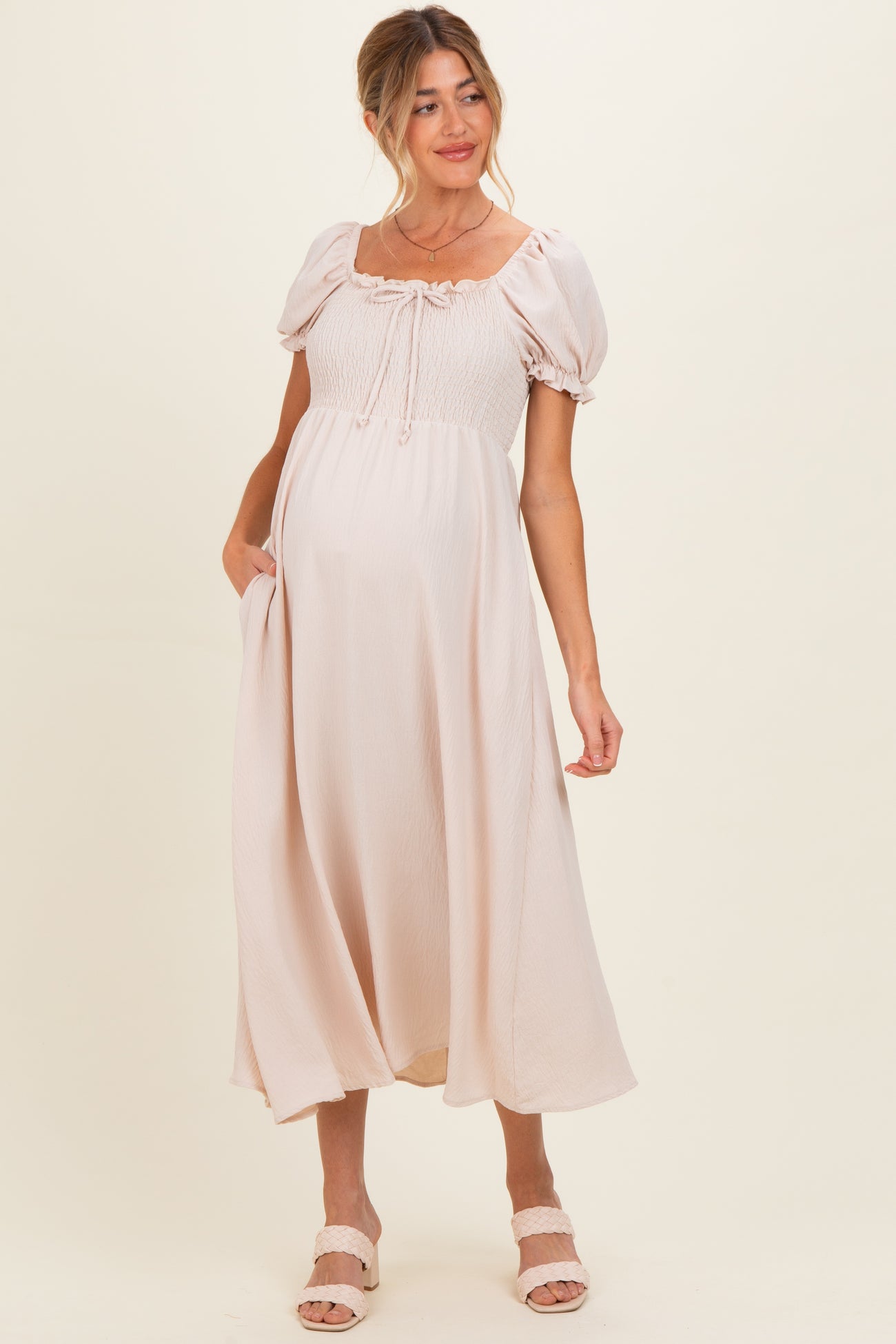 woman wearing a light pink maternity dress with puff sleeves and a tie front, showcasing her baby bump