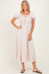 woman wearing a light pink puff sleeve midi dress with a smocked bodice and a tie detail at the neckline