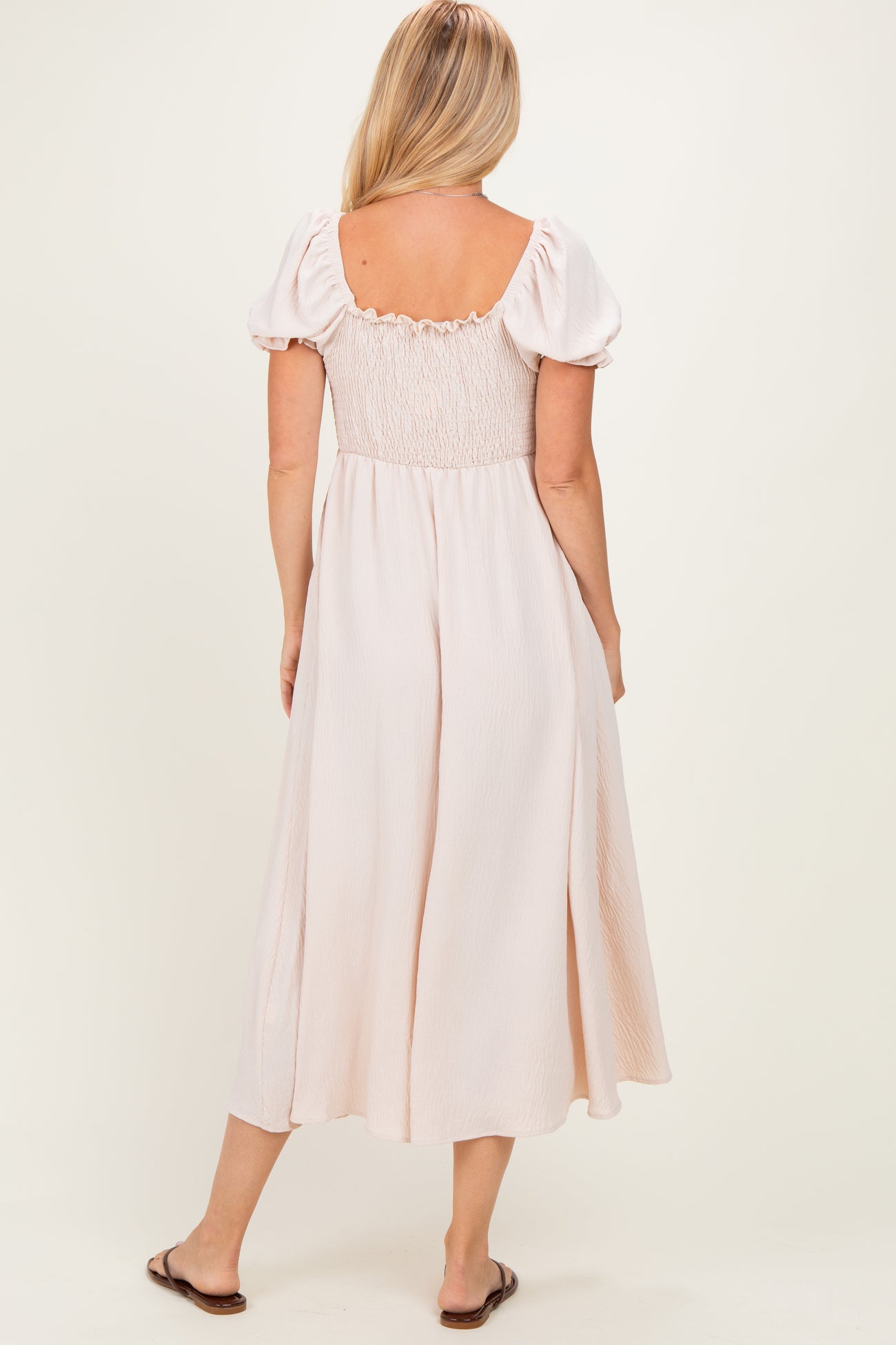 woman wearing a blush pink smocked back dress with puff sleeves, viewed from the back