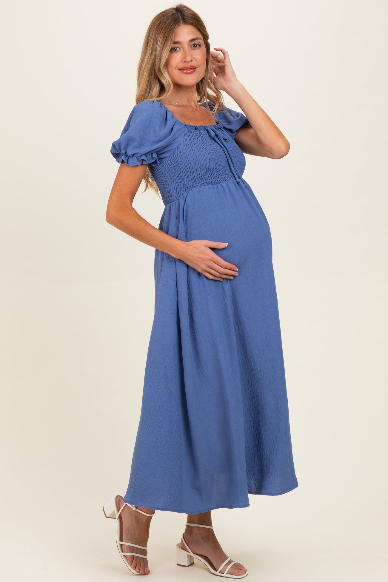 woman wearing a blue maternity maxi dress with puff sleeves and a smocked bodice, holding her baby bump