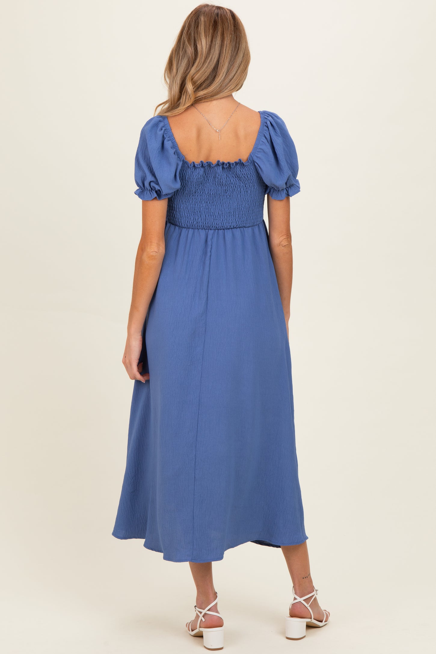 woman wearing a blue maternity dress with short puff sleeves and a smocked back, shown from the back