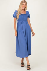 woman wearing a blue smocked maxi dress with puff sleeves and a tie detail at the neckline