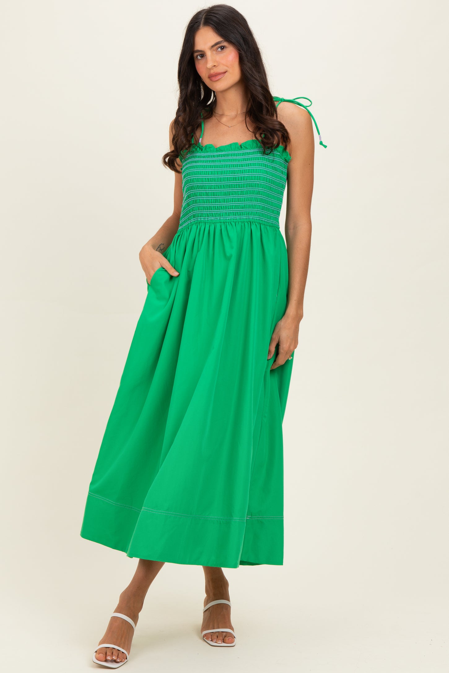 woman wearing a bright green maxi dress with a smocked bodice and adjustable straps, featuring side pockets