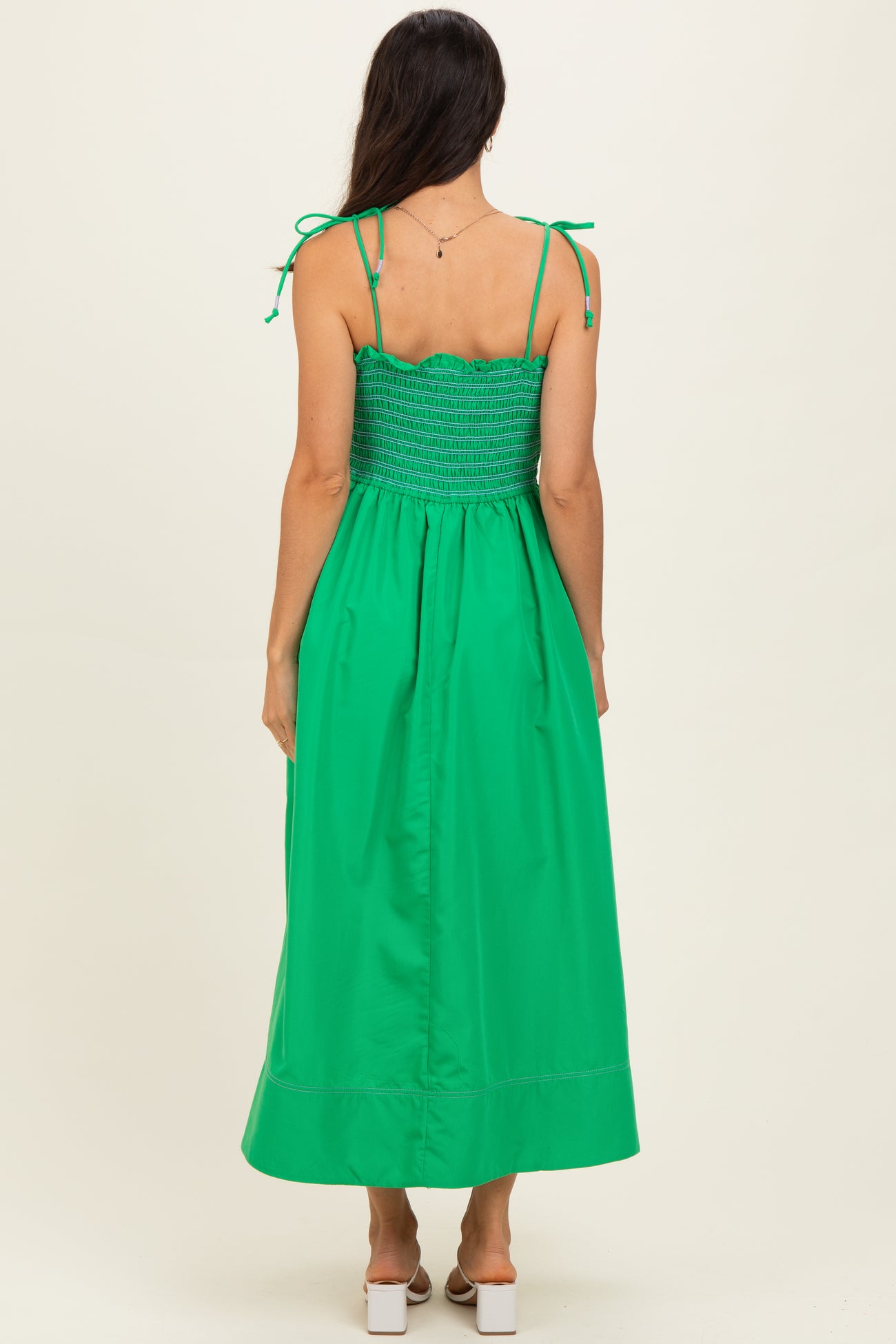 woman wearing a bright green maxi dress with adjustable tie straps and a smocked bodice visible from the back