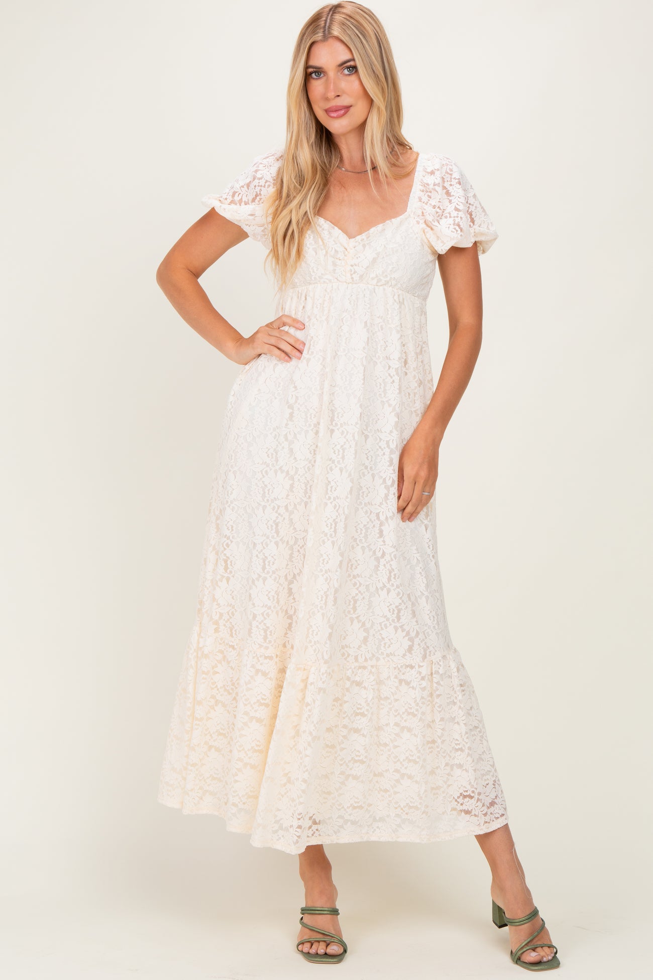 woman wearing a cream lace maxi dress with puff sleeves and a cinched waist, standing with one hand on her hip
