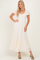 woman wearing a cream lace maxi dress with puff sleeves and a cinched waist, standing with one hand on her hip