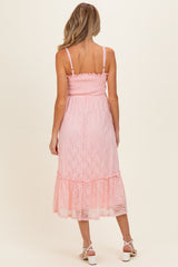 woman wearing a light pink maternity dress with a smocked bodice and lace details, showing off her baby bump