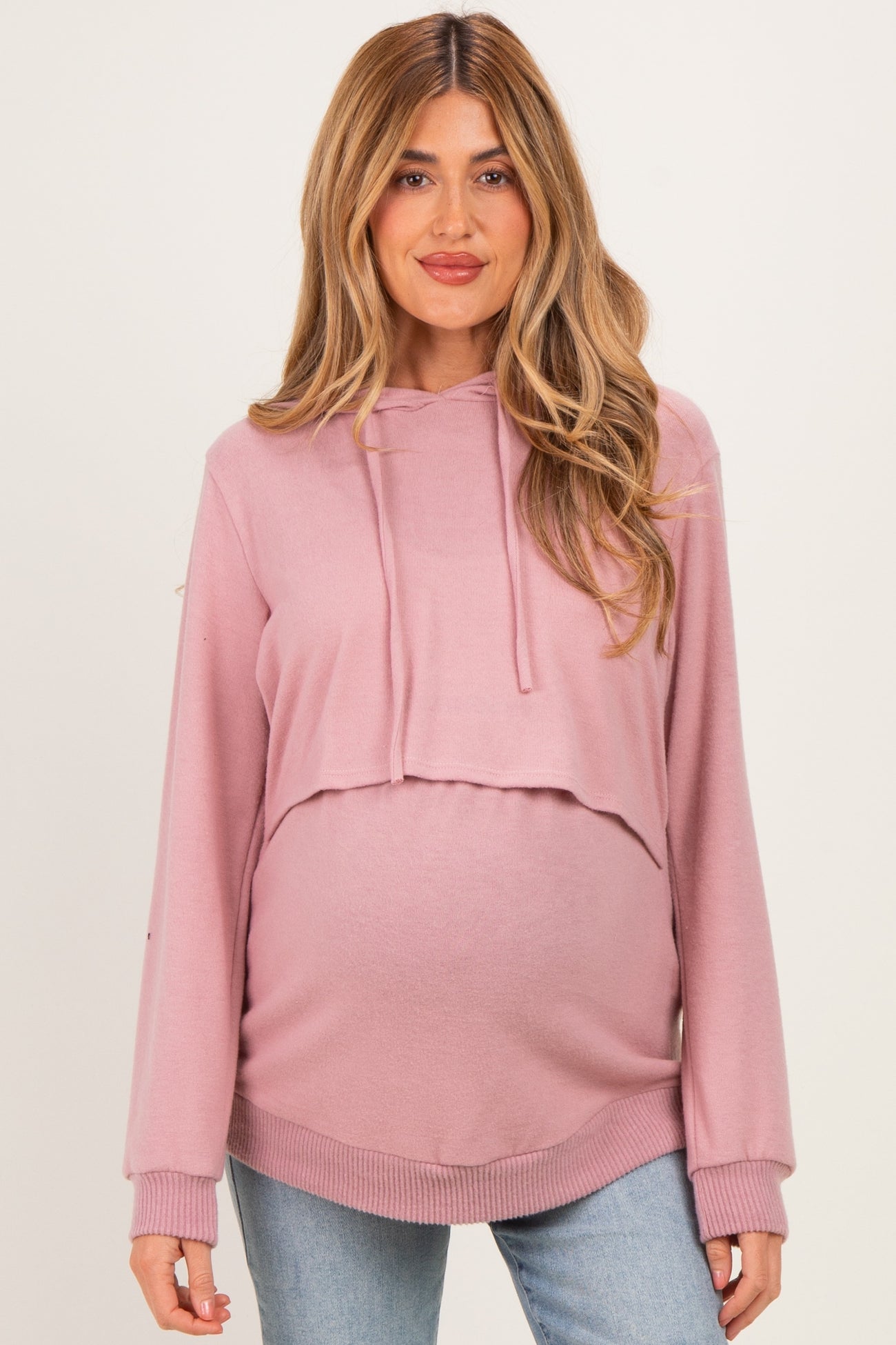 woman wearing a light pink cropped maternity hoodie with a baby bump visible