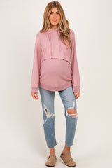 woman wearing a light pink cropped maternity hoodie and distressed blue jeans, showcasing her baby bump
