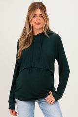 woman wearing a dark green maternity hoodie with a cropped design and a visible baby bump