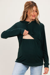 woman wearing a dark green maternity hoodie with a cutout for easy nursing and showing her baby bump