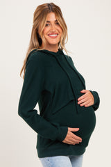 woman wearing a dark green maternity hoodie and holding her baby bump