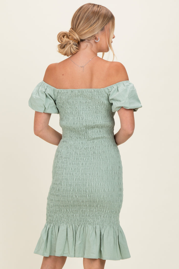 woman wearing a sage green off-the-shoulder fitted dress with smocked bodice and ruffled hem