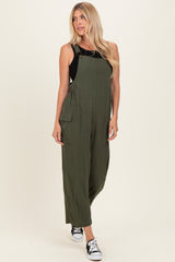 woman wearing an olive green jumpsuit with adjustable straps and side pockets, paired with black sneakers