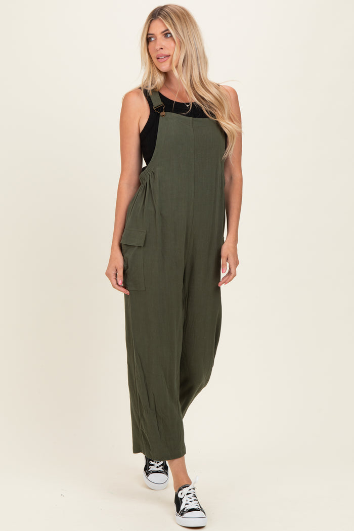 woman wearing an olive green jumpsuit with adjustable straps and side pockets, paired with black sneakers