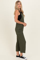 woman wearing a green sleeveless jumpsuit with side pockets and a black top underneath, styled with black sneakers