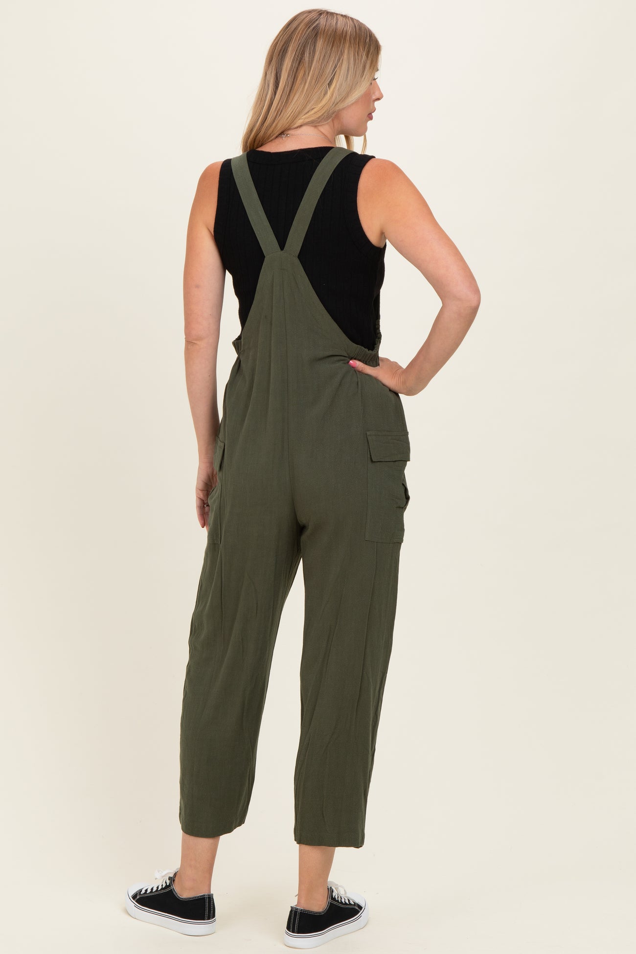 woman wearing an olive green overall jumpsuit with adjustable straps and side pockets, seen from the back