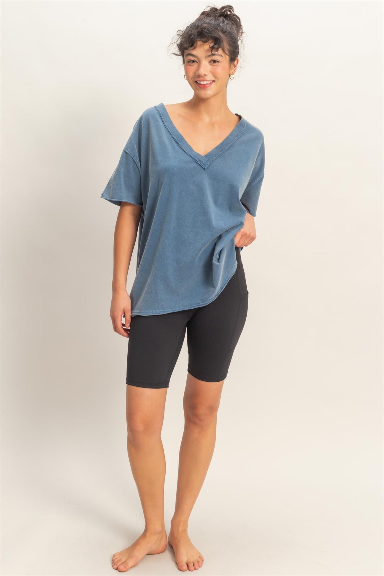 woman wearing a blue oversized v-neck t-shirt with black biker shorts and standing barefoot