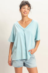 woman wearing a light blue oversized v-neck t-shirt and denim shorts, smiling with one hand in her pocket
