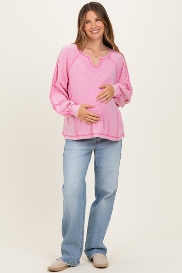 woman wearing a pink long sleeve maternity top and holding her baby bump with light blue jeans