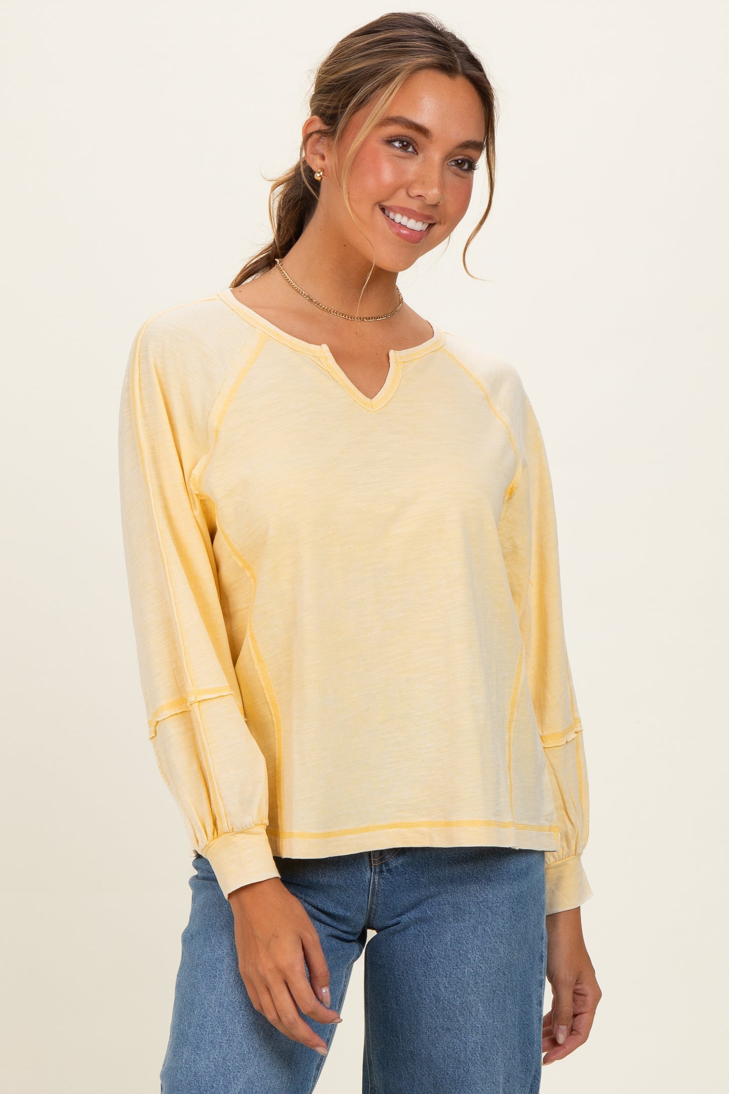 woman wearing a yellow long sleeve top with a v-neck and raglan sleeves, paired with light blue jeans