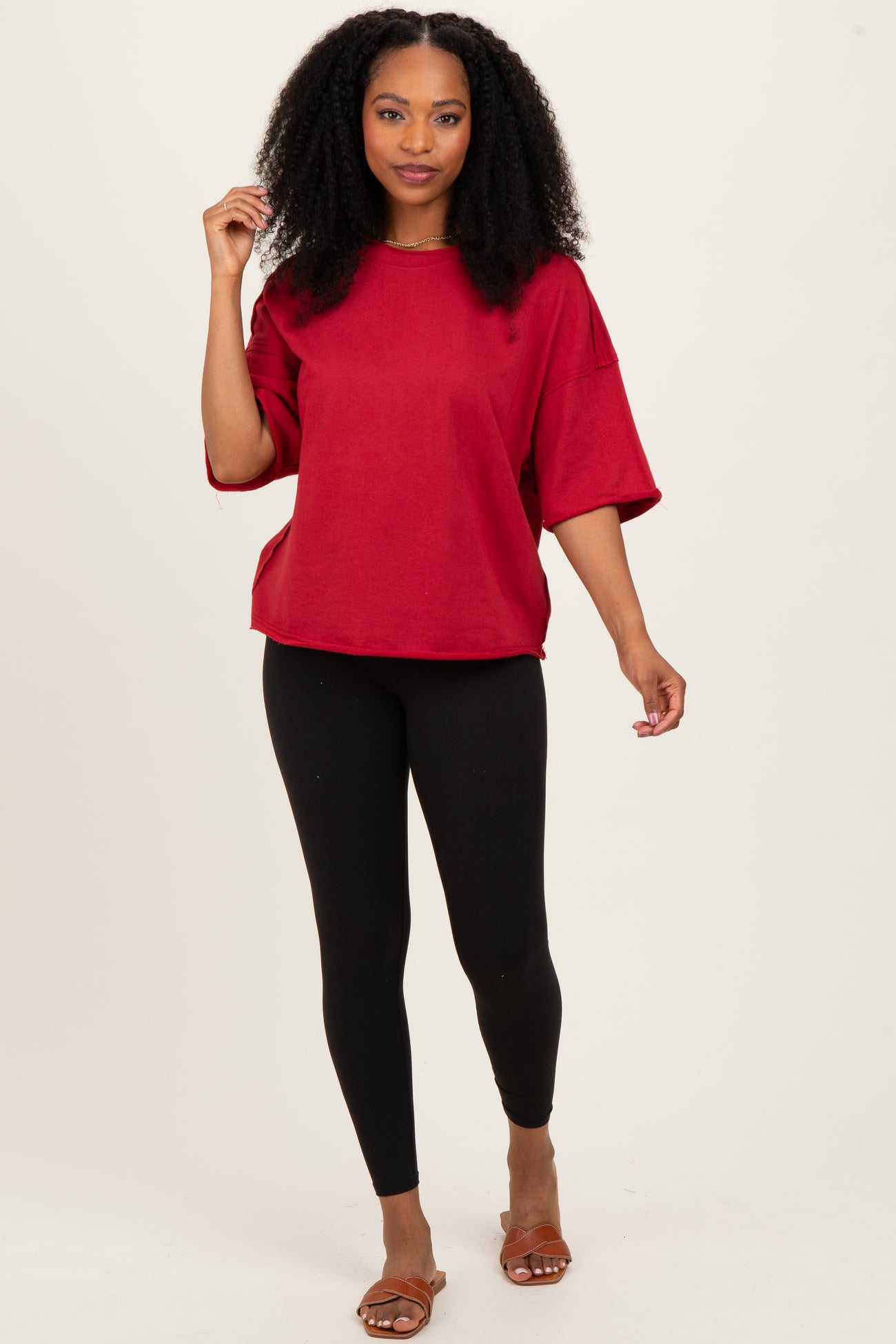 woman wearing a red oversized t-shirt and black leggings, standing and posing with one hand on her hip