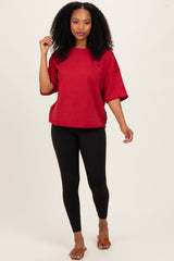 woman wearing a red oversized t-shirt and black leggings, standing and posing with one hand on her hip